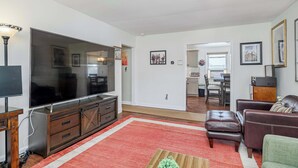 A living room with a large flat-screen TV, wooden entertainment unit, leather sofas, and a red rug. - Flex Comfort Apts of Westchester #2 (Rye Brook)