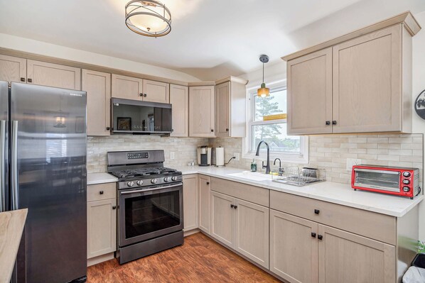 A modern kitchen with stainless steel appliances, light wood cabinets, and a red toaster.