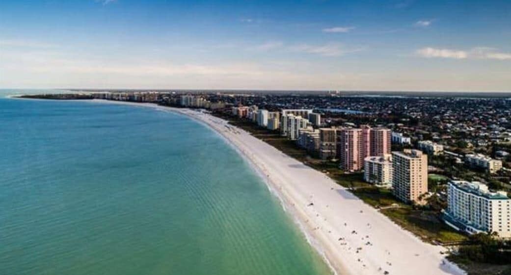 A coastal cityscape with a long beachfront, high-rise buildings, and a clear sky.