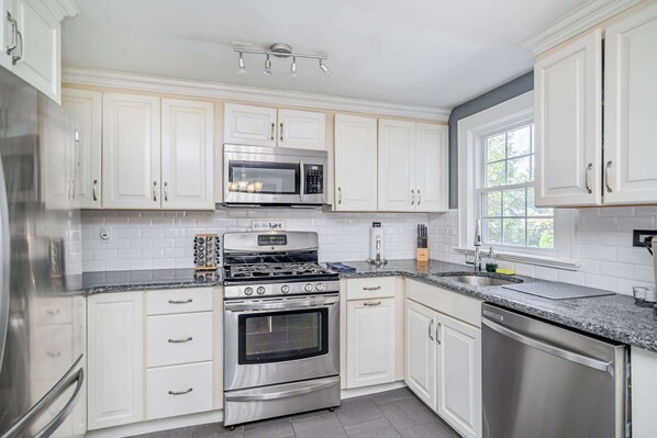A modern kitchen with white cabinets, stainless steel appliances, and a granite countertop.