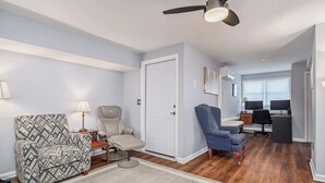 A living room with a ceiling fan, a sofa, a chair, a desk, and a computer setup. - Flex Comfort Apts of Greenwich #1 (Greenwich)