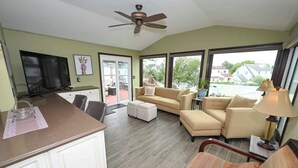 A spacious living area with a sofa set, a television, and a ceiling fan.