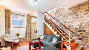 A living room with a stone wall, a staircase, a sofa, a chair, and a table.