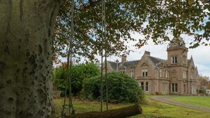 A historic building with a prominent tower and a swing set in a lush garden.
