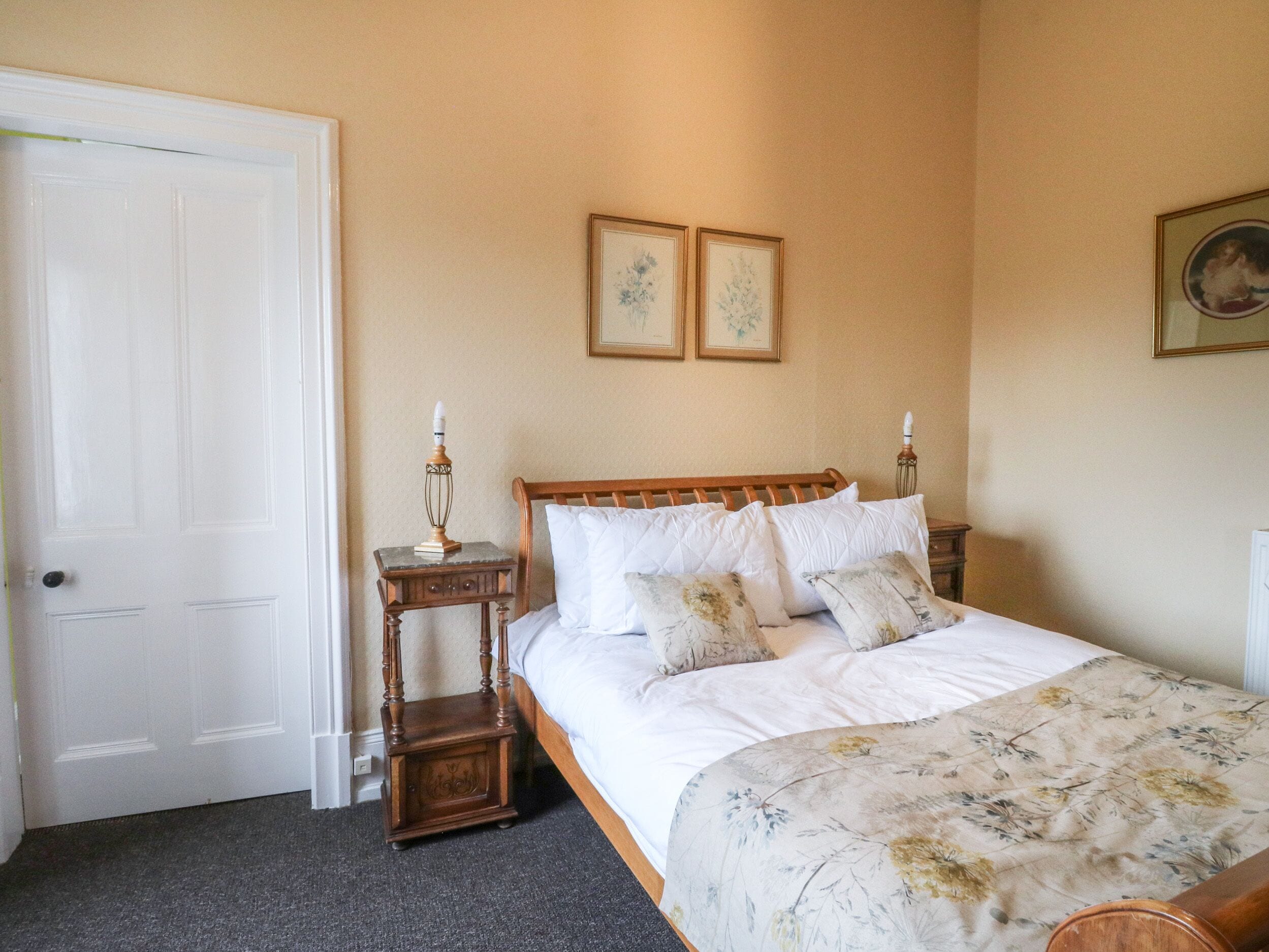 A bedroom with a wooden bed, a nightstand with a lamp, and two framed pictures on the wall.