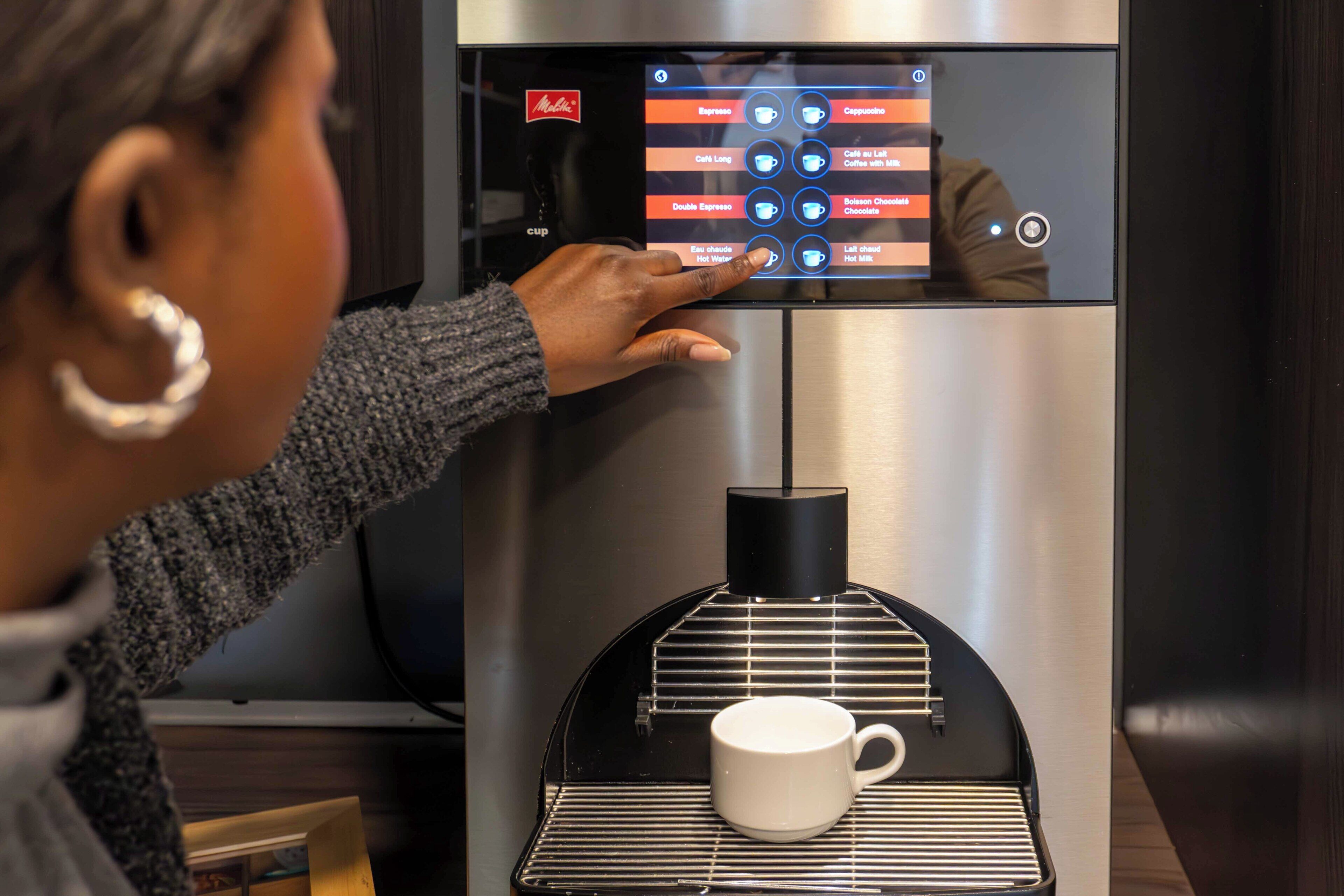 A person interacting with a coffee machine, selecting a beverage option.