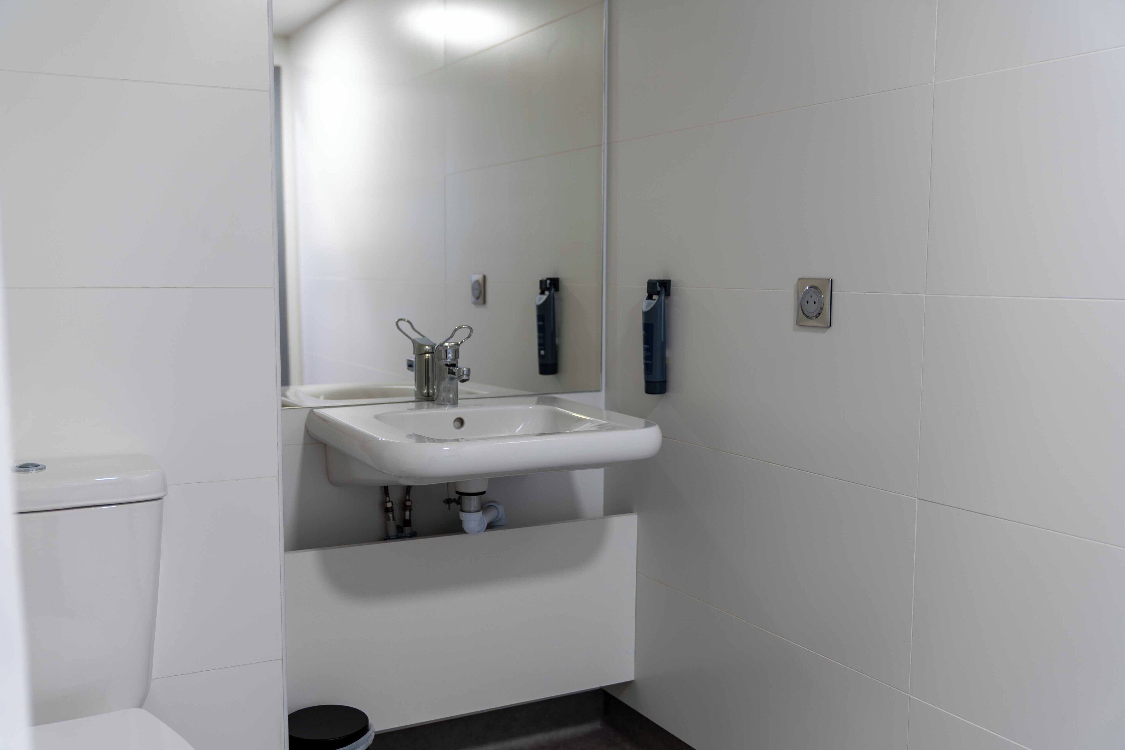 A bathroom with a white sink, mirror, and toilet.