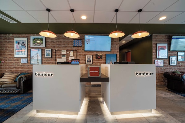 Una zona de recepción con dos letreros que dicen 'bonjour', una pantalla digital y una pared de ladrillo con cuadros enmarcados.