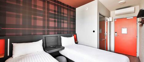 A hotel room with two beds, a red door, and a check-in desk.