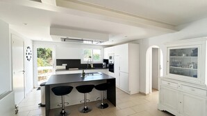 A modern kitchen with a central island, three bar stools, a built-in oven, and a white cabinet with glass doors. - Holiday rental villa with swimming pool in Begur, Casa de Campo (Begur)