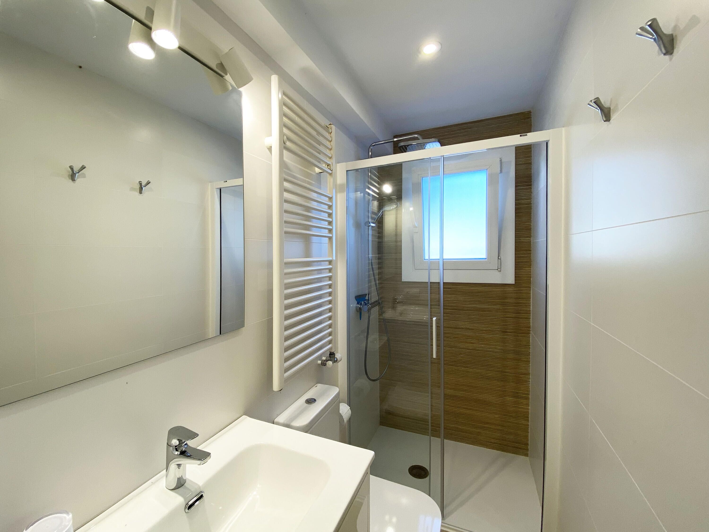 Un baño moderno con ducha de vidrio, un espejo grande y un lavamanos blanco.