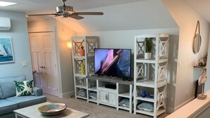 Un salon équipé d’un téléviseur, de meubles blancs, d’un ventilateur de plafond et d’un escalier.