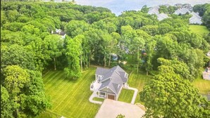An aerial view of a residential area with houses surrounded by lush greenery and a large body of water in the background. - Luxury by the Sea (Southold)