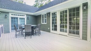 A patio with a table and chairs, a covered area with sliding glass doors, and a building with a dark siding exterior. - Luxury by the Sea (Southold)
