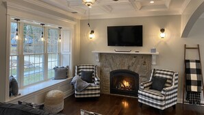 A living room with a fireplace, two armchairs, a sofa, a television, and a ceiling fan. - Luxury by the Sea (Southold)