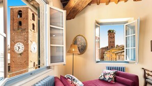 Una habitación con un sofá rojo, una ventana con vista a una torre de ladrillo y un radiador.