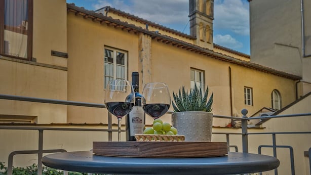 A table with two wine glasses, a bottle, and a potted plant on a balcony. - The Faenza Apartment (Firenze)