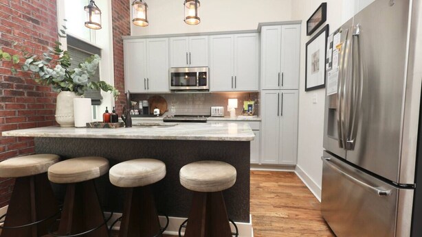 Una cocina con una isla central, taburetes de bar, electrodomésticos de acero inoxidable y una pared de ladrillo.