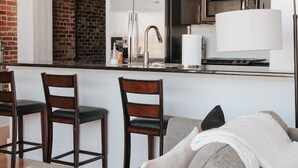A modern kitchen with a central island, a dining area with chairs, and a living space with a sofa. - Glass Loft - Walk to Old City & DT Knox (Knoxville)