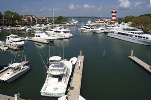 A marina with multiple boats docked, a lighthouse in the background, and a clear sky.