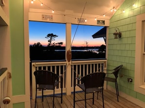 A porch with two chairs, a string of lights, and a view of a sunset over a body of water.