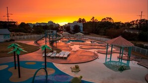 Un parc infantil amb tobogans i elements per escalar, envoltat per una tanca i un porxo.