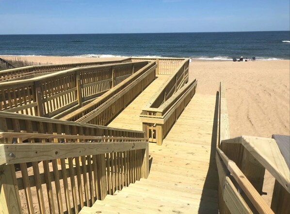 A wooden boardwalk leading to a sandy beach with the ocean in the background.
