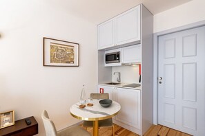 Une cuisine compacte avec des meubles blancs, un four à micro-ondes et un évier. On y trouve une table ronde avec des chaises et une carte encadrée accrochée au mur.