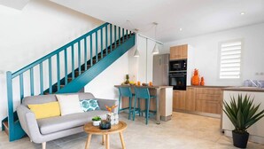 Un appartamento moderno con divano grigio, una scala color petrolio, cucina con mobili in legno e zona pranzo con uno sgabello da bar.