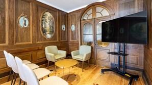 A room with wooden paneled walls, a large flat-screen TV, and a seating area with chairs and a small round table. - Lp Heritage 2. 01 W/ city view - sé apartamentos (Braga)