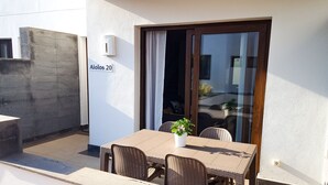An outdoor patio with a table and chairs, a potted plant, and a sliding glass door. - AIOLOS 20 by Buenavilla|Great apartment in the marina of Puerto Calero (Las Palmas)
