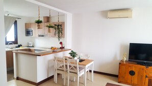 A modern kitchen with a central island, white chairs, a dining table, and a TV on a wooden cabinet. - AIOLOS 20 by Buenavilla|Great apartment in the marina of Puerto Calero (Las Palmas)