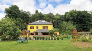 A yellow house with a stone facade, surrounded by a well-maintained lawn and trees. - The Woodlands Lower Level (Narberth)