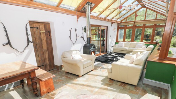 A sunlit room with a fireplace, leather sofas, and a wooden table. - The Woodlands Lower Level (Narberth)