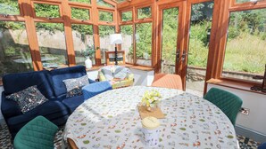 A conservatory with a round table, blue and green chairs, and a patterned tablecloth. - The Woodlands Lower Level (Narberth)