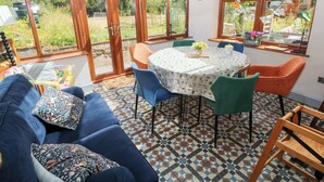 A sunroom with a large glass door, a round table, blue and orange chairs, and a patterned floor. - The Woodlands Lower Level (Narberth)