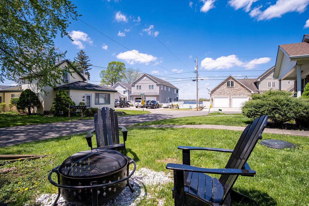 A residential street with houses, a barbecue grill, and two Adirondack chairs.