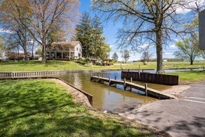 A riverside walkway with a wooden bridge, a gazebo, and a house in the background.