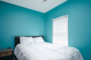 A bedroom with teal walls, a white bed, and a window with blinds.
