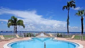 Ein Pool mit Blick auf den Ozean, umgeben von Palmen und Liegestühlen.