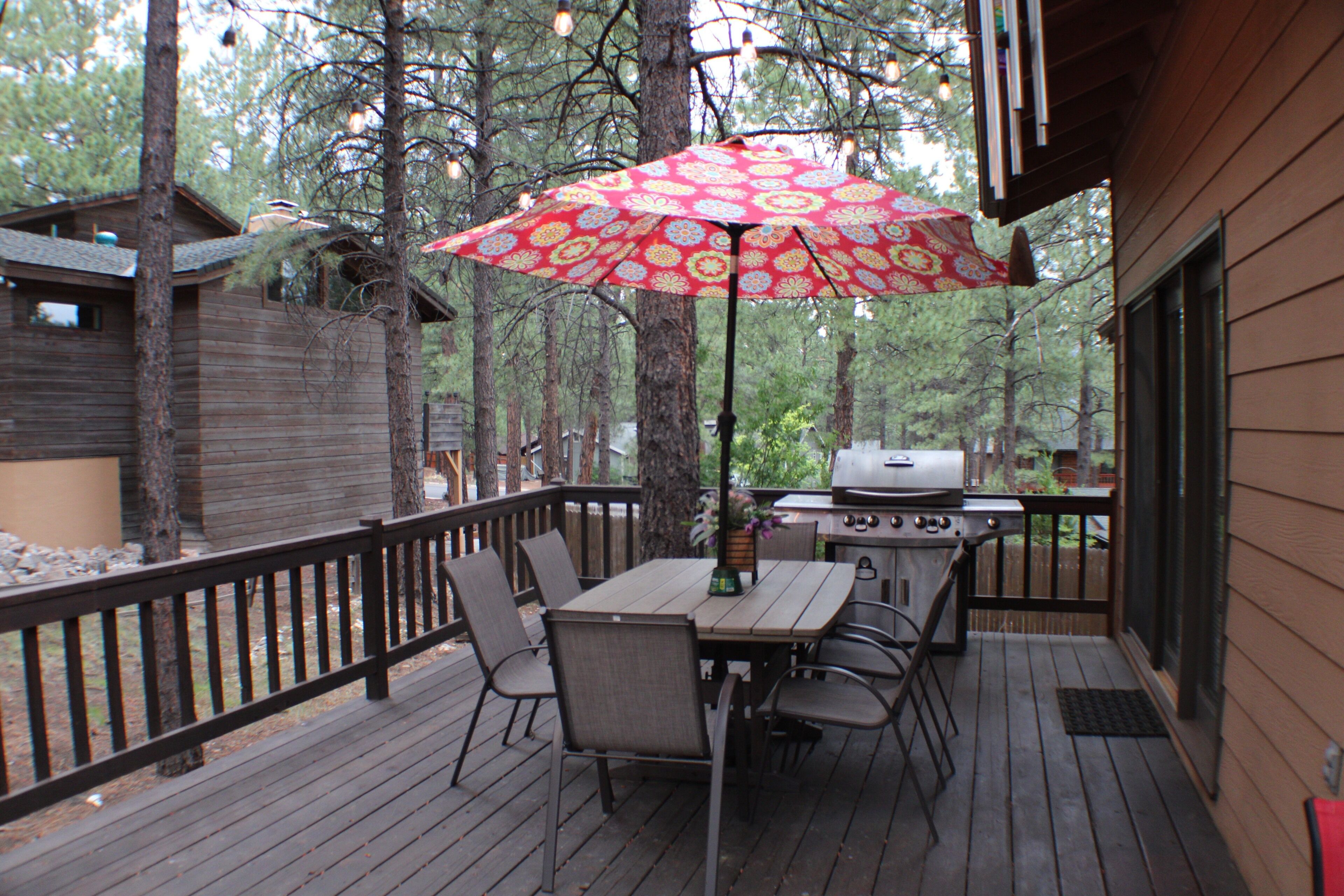 A wooden deck with a table and chairs, a grill, and a red umbrella.