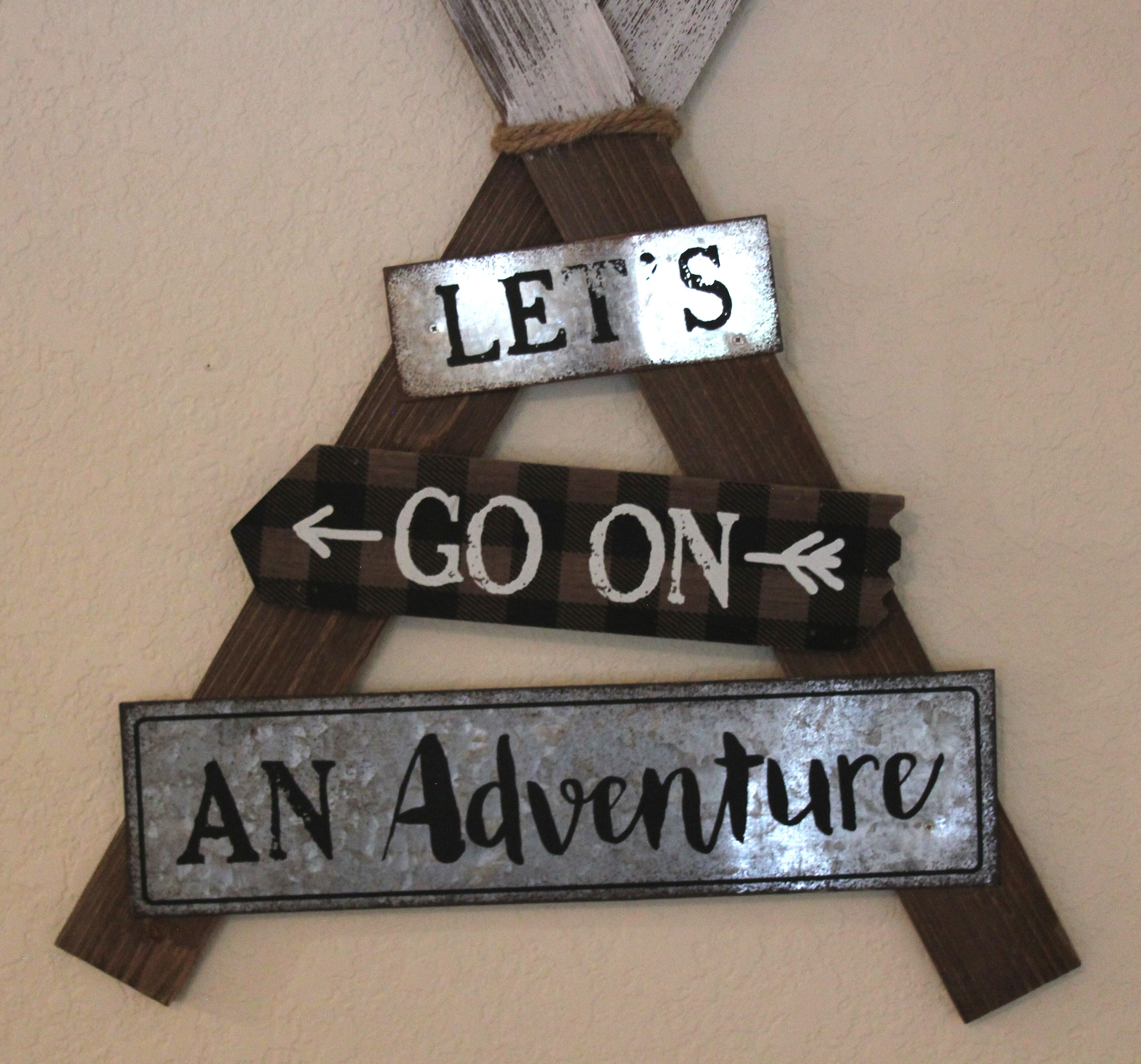Een houten bord met de tekst 'LET'S GO ON AN Adventure' bevestigd aan een muur.