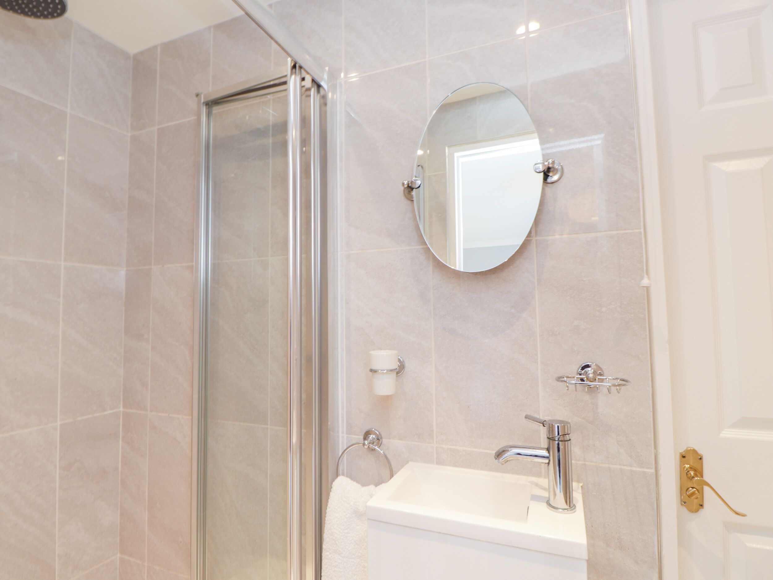 A bathroom with a glass shower enclosure, a sink with a chrome faucet, and a round mirror on the wall.