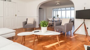 En moderne stue med en hvid sofa, to lænestole, et sofabord og et fjernsyn på et stativ.