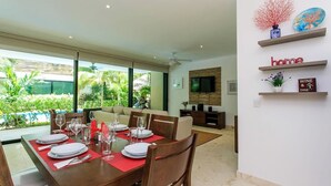 A dining area with a table set for six, a TV mounted on the wall, and a view of a swimming pool. - Poolfront Tulum Condo! Near Mayan Ruins & Beach by Stella Rentals (Tulum)