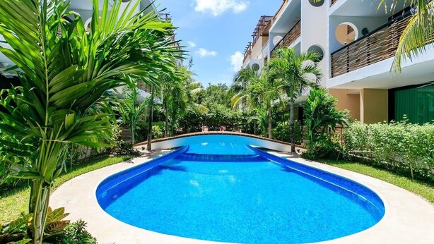 A swimming pool surrounded by lush greenery and modern buildings. - Poolfront Tulum Condo! Near Mayan Ruins & Beach by Stella Rentals (Tulum)