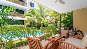 A poolside area with wooden furniture, a ceiling fan, and a view of a swimming pool surrounded by tropical plants. - Poolfront Tulum Condo! Near Mayan Ruins & Beach by Stella Rentals (Tulum)