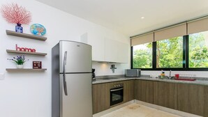 A modern kitchen with a stainless steel refrigerator, wooden cabinets, a built-in oven, and a window with a view of greenery. - Poolfront Tulum Condo! Near Mayan Ruins & Beach by Stella Rentals (Tulum)