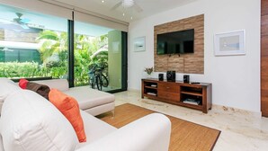 A modern living room with a sofa, a TV mounted on a wooden wall, and a balcony with a bicycle. - Poolfront Tulum Condo! Near Mayan Ruins & Beach by Stella Rentals (Tulum)
