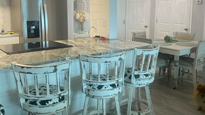 Una cocina moderna con una isla central, taburetes de bar y una zona de comedor con sillas.